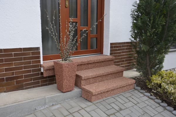 Schodiště obložené betonovými schodišťovými prvky ve vymývaném povrchu ORANŽ červená s květináčem ZARA u vchodu